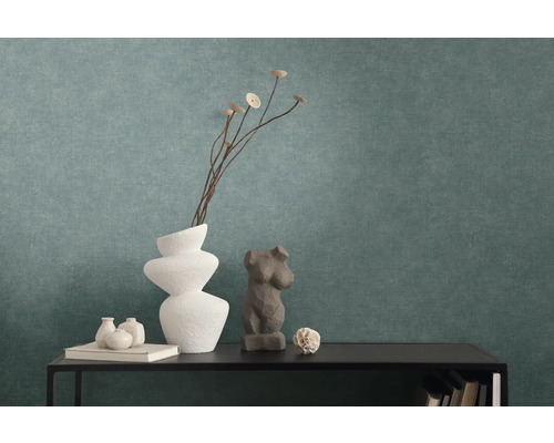 Papier peint intissé texturé de couleur pétrole derrière une console noire avec des vases décoratifs et des sculptures.