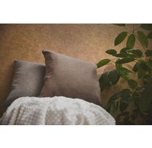 Deux coussins décoratifs et une couverture texturée devant un papier peint à motifs à côté d'une plante d'intérieur.