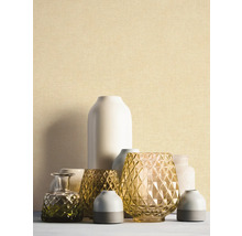 Papier peint à structure fine beige clair derrière un groupe de vases décoratifs en verre et en céramique.