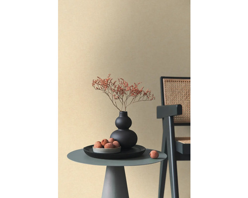 Papier peint intissé beige à texture fine dans une pièce minimaliste avec table d'appoint, vase noir et chaise en rotin.