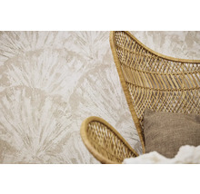 Papier peint texturé avec un motif de feuilles de palmier en éventail derrière un fauteuil en rotin tressé avec un coussin en tissu.