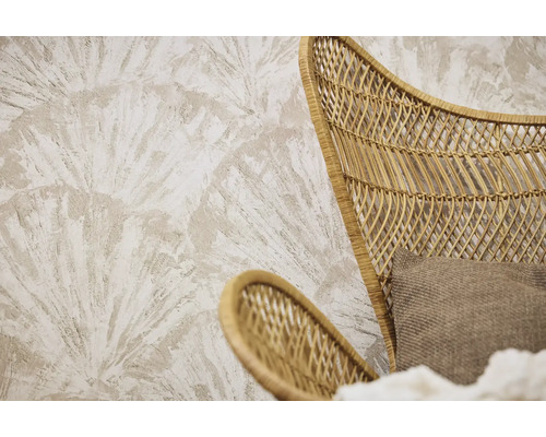 Papier peint texturé avec un motif de feuilles de palmier en éventail derrière un fauteuil en rotin tressé avec un coussin en tissu.