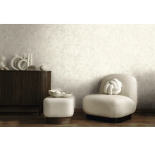 Salon moderne avec papier peint clair à motifs, buffet en bois sombre, fauteuil rembourré clair et pouf assorti.
