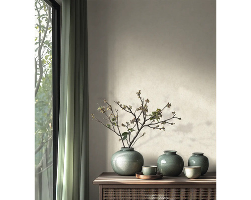 Salon lumineux avec buffet en bois, vases en céramique verte avec des branches devant un mur à peinture structurée et des rideaux.