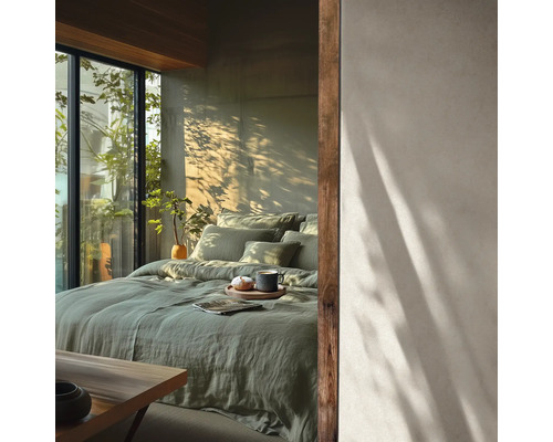 Chambre lumineuse avec linge de lit en lin vert, grandes fenêtres et ombres de plantes sur le mur. Style minimaliste.