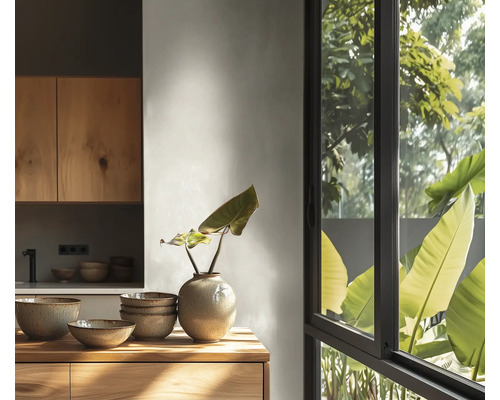 Cuisine lumineuse avec meubles en bois, bols en céramique et vase sur un plan de travail en bois devant une grande fenêtre donnant sur des plantes.
