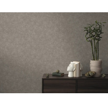 Papier peint intissé texturé aspect béton sur un mur derrière un buffet sombre avec des livres et une plante en pot.