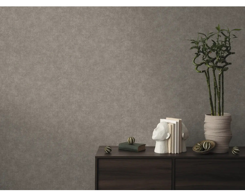 Papier peint intissé texturé aspect béton sur un mur derrière un buffet sombre avec des livres et une plante en pot.