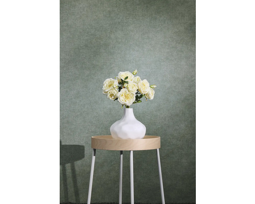Papier peint intissé structuré vert avec aspect textile derrière une table d'appoint avec un vase à fleurs.