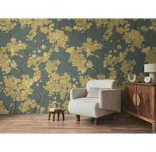 Papier peint intissé avec branches fleuries jaunes sur fond sombre dans un salon avec fauteuil clair et meubles en bois sur sol stratifié.