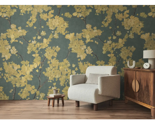 Papier peint intissé avec branches fleuries jaunes sur fond sombre dans un salon avec fauteuil clair et meubles en bois sur sol stratifié.