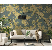 Salon avec papier peint intissé au motif floral, fleurs jaunes sur fond vert foncé, canapé gris clair et lampadaire à arc noir.