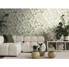 Salon lumineux avec papier peint à motif botanique, canapé modulaire blanc, table en verre avec boules de pierre et plantes d'intérieur.
