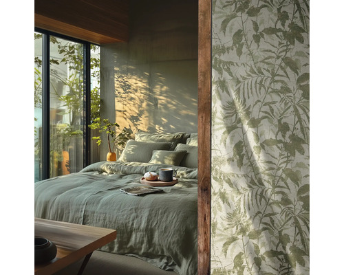 Chambre avec literie en lin vert clair et papier peint à motif de feuilles botaniques devant une fenêtre ensoleillée.