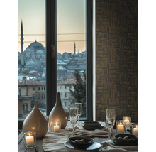 Eleganter Esstisch mit brennenden Kerzen, Keramikvasen und Gläsern vor einem Fenster mit Stadtansicht auf Moscheen. Geometrische Tapete.
