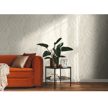 Salon lumineux avec papier peint au motif de feuilles beiges, canape orange avec coussins et petite table avec plante verte.
