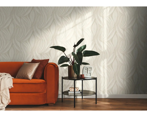 Salon lumineux avec papier peint au motif de feuilles beiges, canape orange avec coussins et petite table avec plante verte.