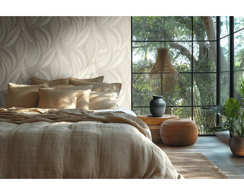 Chambre à coucher lumineuse avec papier peint à motif de feuilles, lit avec housse en lin, grande fenêtre et éléments de décoration naturels.