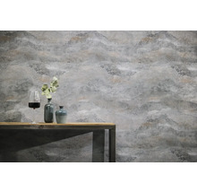 Papier peint intissé structuré à aspect pierre sur un mur derrière une table en bois avec des vases décoratifs et un verre de vin.