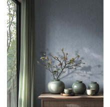 Trois vases en céramique verte avec glaçure craquelée et une branche fleurie sur un buffet en bois devant un mur bleu-gris texturé.
