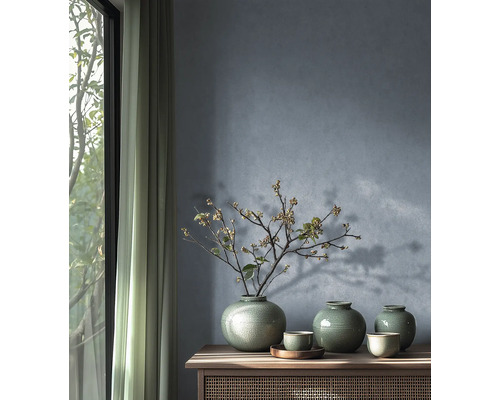 Trois vases en céramique verte avec glaçure craquelée et une branche fleurie sur un buffet en bois devant un mur bleu-gris texturé.