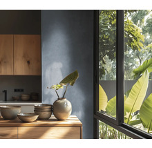 Cuisine moderne avec meubles en bois, vaisselle en céramique sur plan de travail en bois, mur texturé et grande fenêtre avec vue sur les plantes.