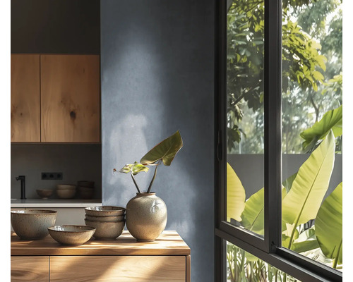 Cuisine moderne avec meubles en bois, vaisselle en céramique sur plan de travail en bois, mur texturé et grande fenêtre avec vue sur les plantes.