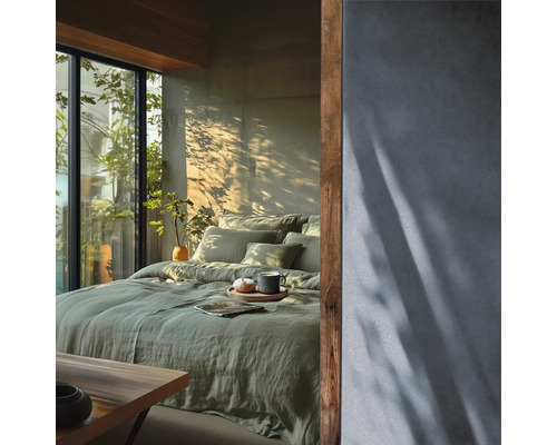 Chambre lumineuse avec parure de lit en lin vert, mur texture et accents en bois a cote d une fenetre avec vue sur la verdure.