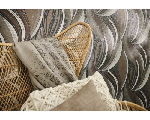 Papier peint intissé à motif de grandes feuilles dans des tons de terre derrière un fauteuil en rotin tressé avec coussins.
