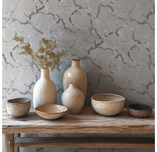Décoration rustique avec vases et bols en céramique sur un banc en bois devant un papier peint à motifs de branches fleuries.