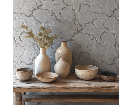 Décoration rustique avec vases et bols en céramique sur un banc en bois devant un papier peint à motifs de branches fleuries.