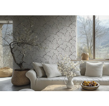Papier peint intissé avec un motif de branches et de fleurs délicat sur un mur dans un salon clair derrière un canapé avec des coussins.