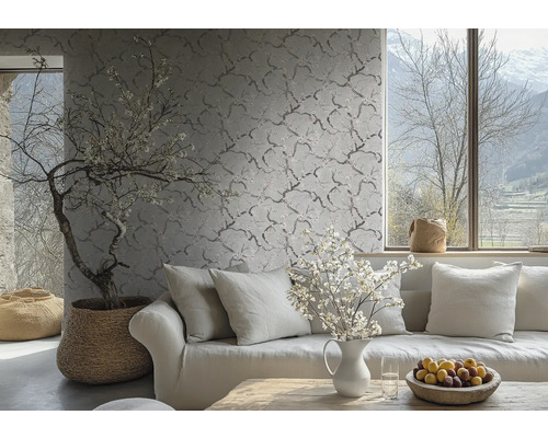 Papier peint intissé avec un motif de branches et de fleurs délicat sur un mur dans un salon clair derrière un canapé avec des coussins.