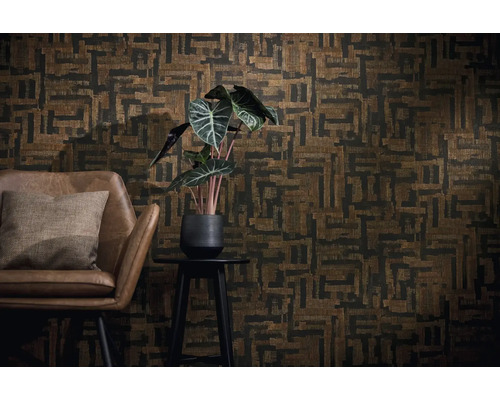 Décoration murale avec papier peint géométrique marron et noir, fauteuil en cuir marron avec coussin et plante verte sur un guéridon.