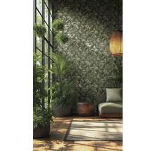 Papier peint intissé avec motif de feuilles tropicales vert et crème dans une pièce lumineuse avec plantes, canapé vert et suspension tressée.