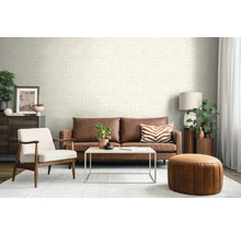 Salon moderne avec papier peint crème texturé, canapé en cuir marron, fauteuil blanc et pouf en cuir rond.