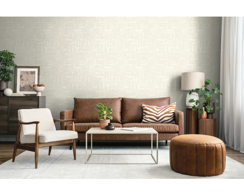 Salon moderne avec papier peint crème texturé, canapé en cuir marron, fauteuil blanc et pouf en cuir rond.