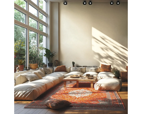 Salon lumineux avec grand canapé modulable, table basse en bois et tapis oriental devant de grandes fenêtres et des spots au plafond.