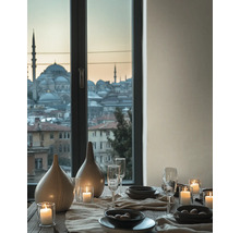 Table dressée avec vases en céramique, verres et bougies devant une fenêtre avec vue sur une ville avec des mosquées au crépuscule.