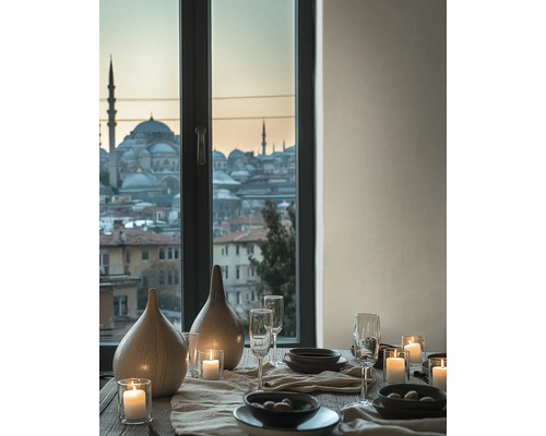 Table dressée avec vases en céramique, verres et bougies devant une fenêtre avec vue sur une ville avec des mosquées au crépuscule.