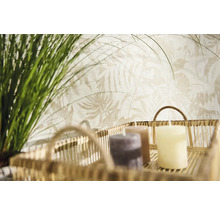 Papier peint intissé avec motif de feuilles botaniques claires derrière un panier décoratif avec bougies et herbes vertes.