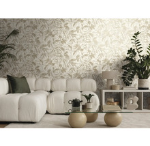 Salon lumineux avec papier peint intissé à motif de feuilles, canapé modulaire blanc en tissu bouclé et table basse en verre avec pieds en pierre.