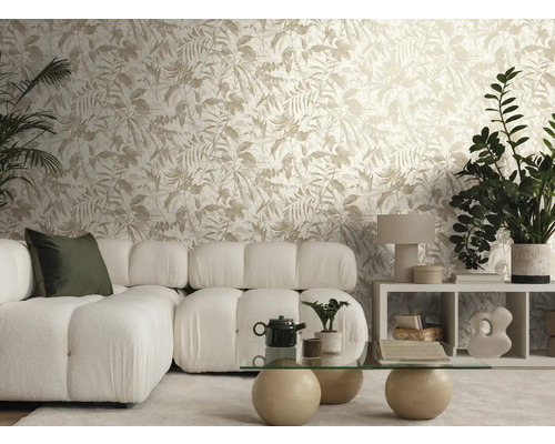Salon lumineux avec papier peint intissé à motif de feuilles, canapé modulaire blanc en tissu bouclé et table basse en verre avec pieds en pierre.