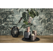 Papier peint intissé avec motif de jungle et structure vintage derrière une plante Alocasia en pot de céramique et une lanterne grillagée sur bois.