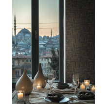 Gedeckter Tisch mit Kerzen und Vasen vor einem Fenster mit Stadtblick und Wand mit geometrisch gemusterter Tapete.