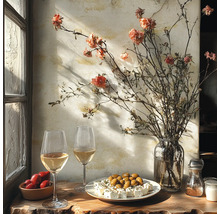 Table rustique près d'une fenêtre avec vin blanc, olives, féta, tomates et un vase de fleurs séchées devant un mur texturé.