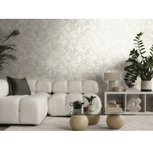 Salon lumineux avec papier peint intissé au motif de feuilles, canapé modulable, table en verre et plantes d'intérieur.