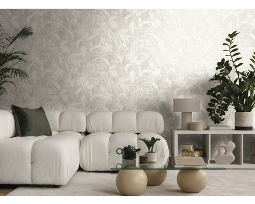 Salon lumineux avec papier peint intissé au motif de feuilles, canapé modulable, table en verre et plantes d'intérieur.