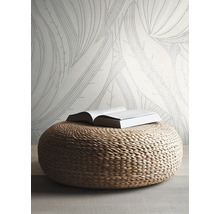 Papier peint intissé à grandes feuilles dans une pièce claire et moderne avec un pouf tressé en matériau naturel.