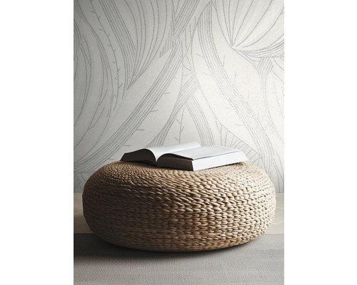 Papier peint intissé à grandes feuilles dans une pièce claire et moderne avec un pouf tressé en matériau naturel.